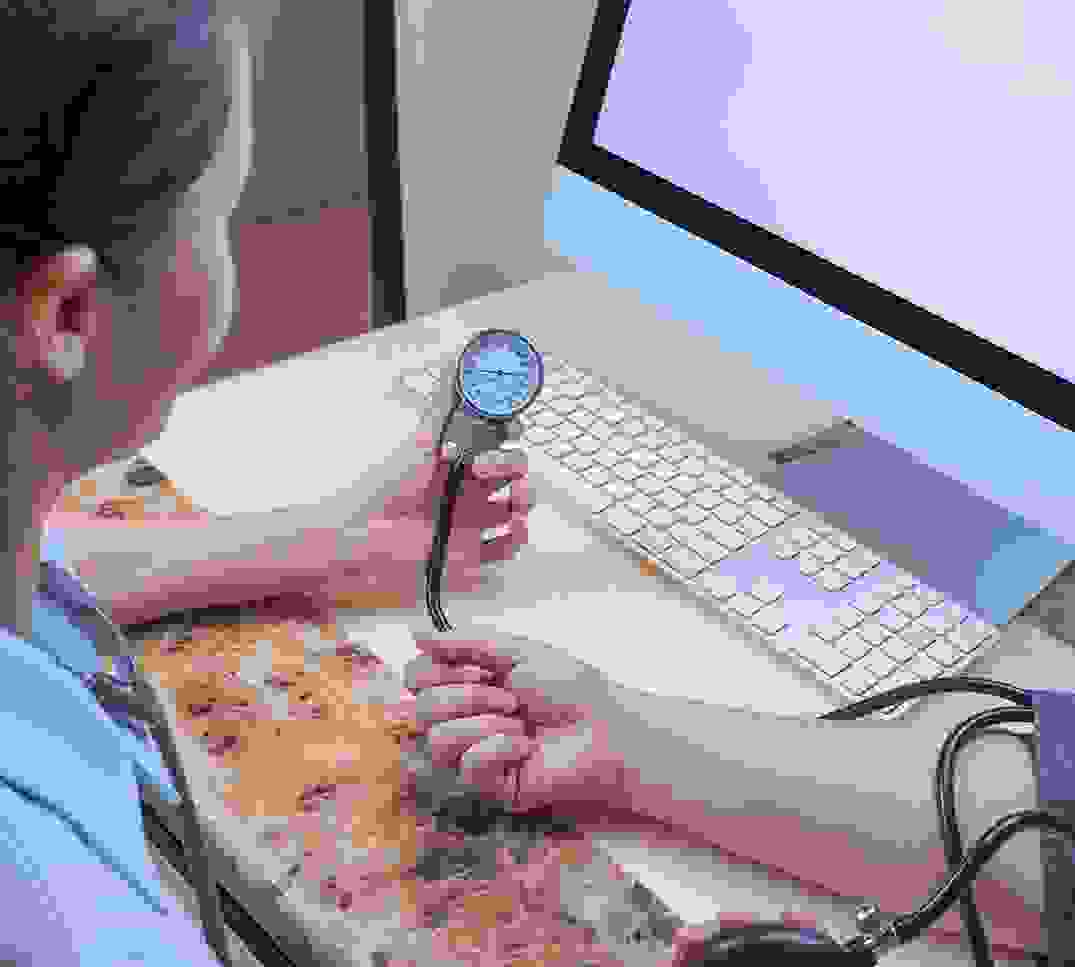 Ärztin misst Blutdruck am Arbeitsplatz mit Computer - Digitalisierung im Schweizer Gesundheitswesen durch TARDOC Reform 2026